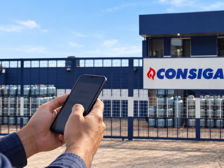 Mãos de cliente com celular diante de um depósito de gás