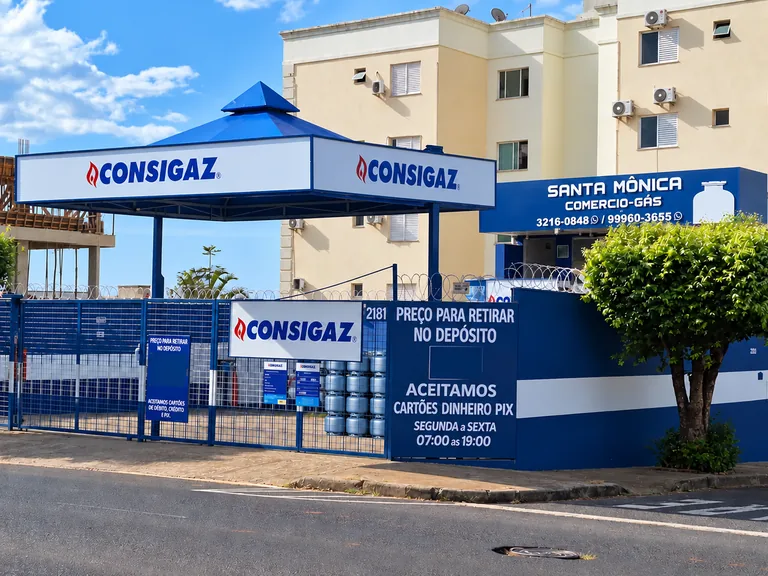 Fachada da Hiper-Gás vista em três quartos, com entrada do depósito e placas da Consigaz e Santa Mônica
